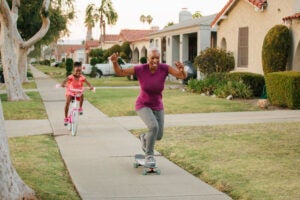 A woman with a reverse mortgage in California skateboards down the sidewalk with her grandaughter following on a bike