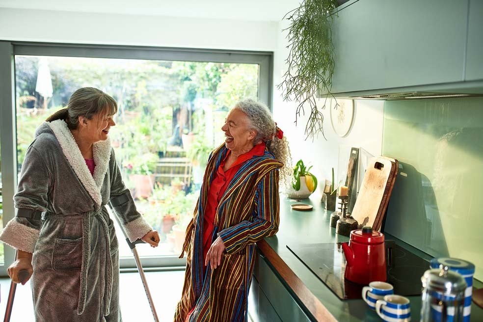 Two older women laughing in a kitchen