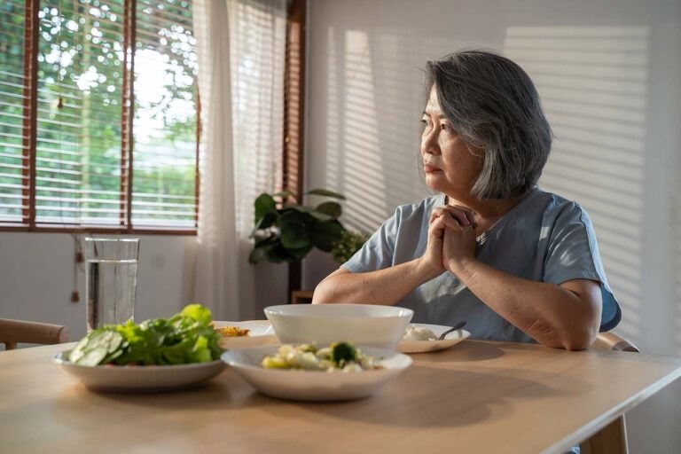 A woman sits a lone at a table thinking about divorce and her reverse mortgage