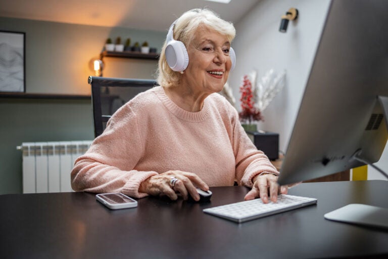 A tech savvy senior using a home computer with headphones